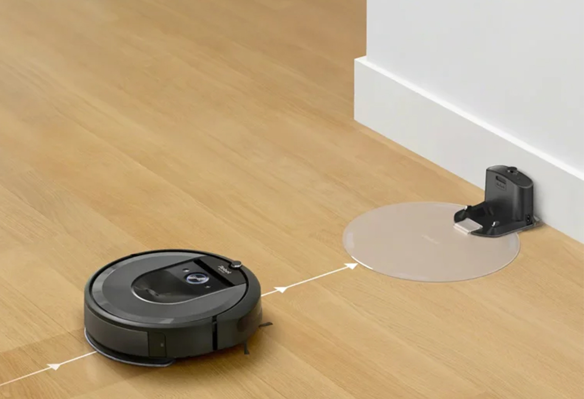 απεικονίζεται η σκούπα robot η οποία πηγαίνει στην βάση για φόρτιση, ενώ στο πάτωμα διαγράφονται άσπρα βέλη που δείχνουν την πορεία της.